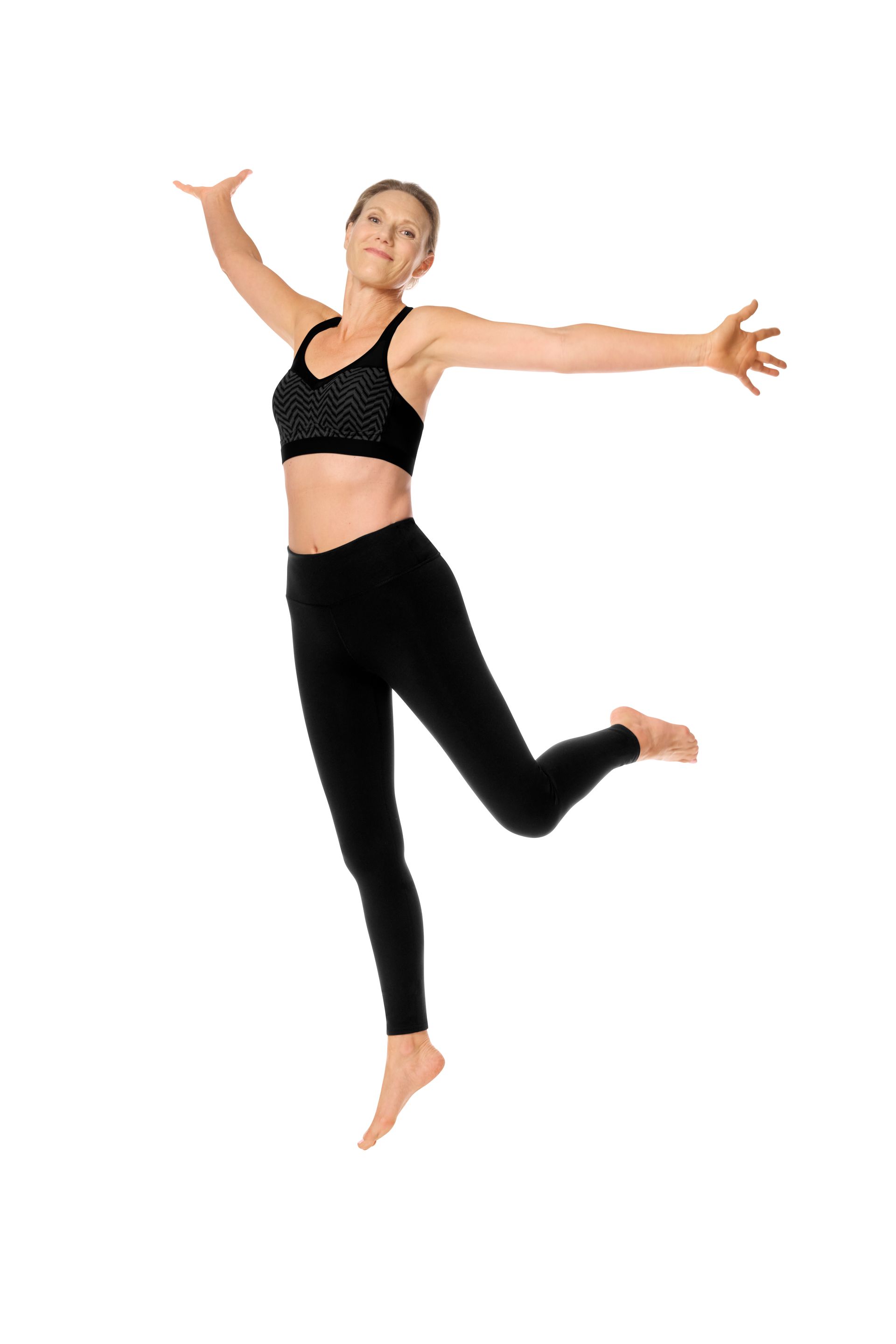Woman leaping in air, arms outstretched, wearing black athletic wear, smiling.