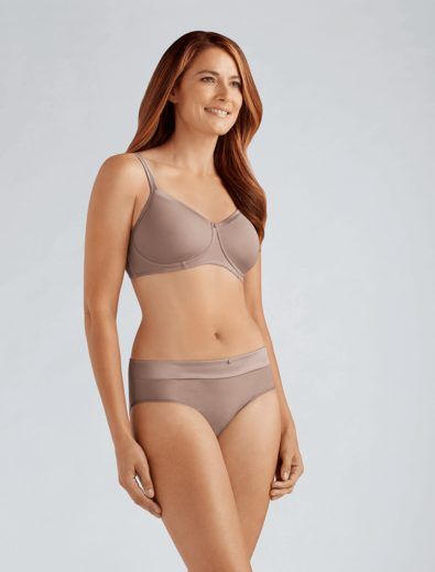 Woman in nude-colored bra and underwear, smiling, standing in front of a neutral backdrop.