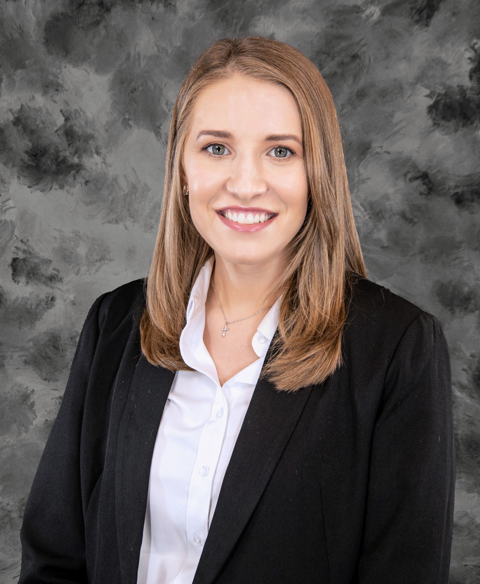 Woman in black blazer, white shirt, smiling, against a mottled gray backdrop.