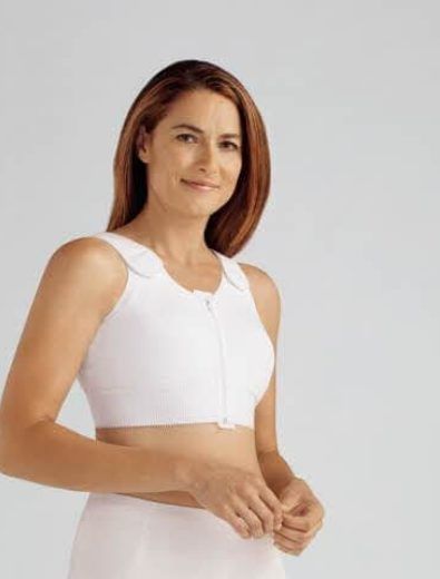 Woman wearing a white post-surgical bra, smiling, standing in a studio.