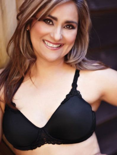 Woman smiling, wearing a black bra, seated on wooden stairs.