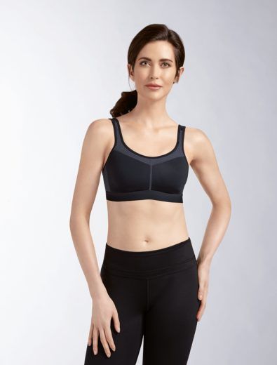 Woman wearing a black sports bra and leggings, standing in a studio setting.