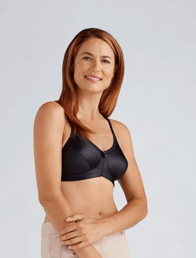 Woman in a black bra, smiling, arms crossed over stomach. Light background.