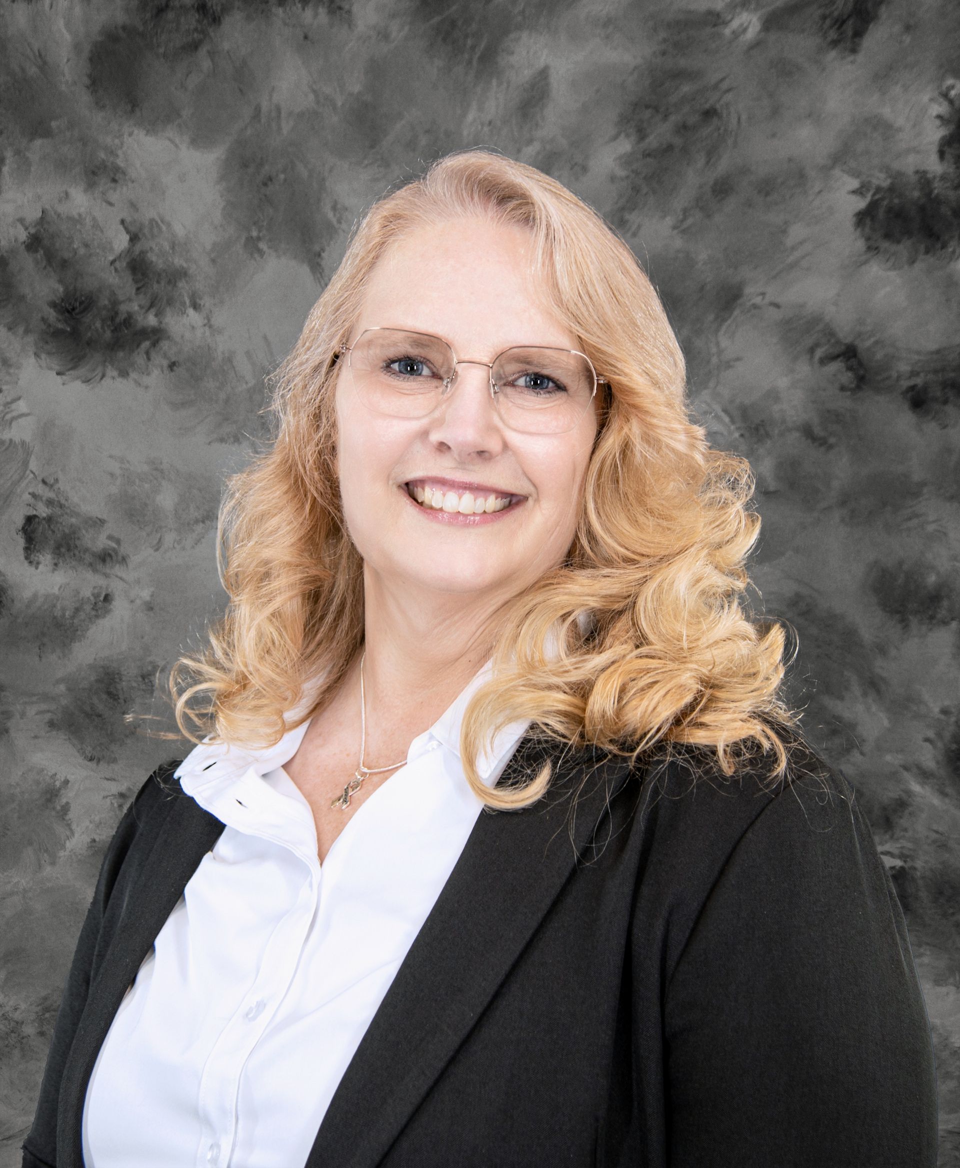 Woman with blonde hair wearing glasses, a white shirt, and a black blazer, smiling at the camera.