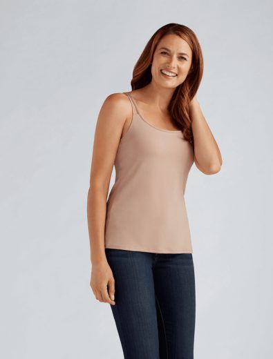 Woman in a tan camisole and jeans smiles, hand in hair.