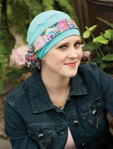 Woman wearing a turquoise head covering with floral trim, smiling, in a denim jacket, outdoors.