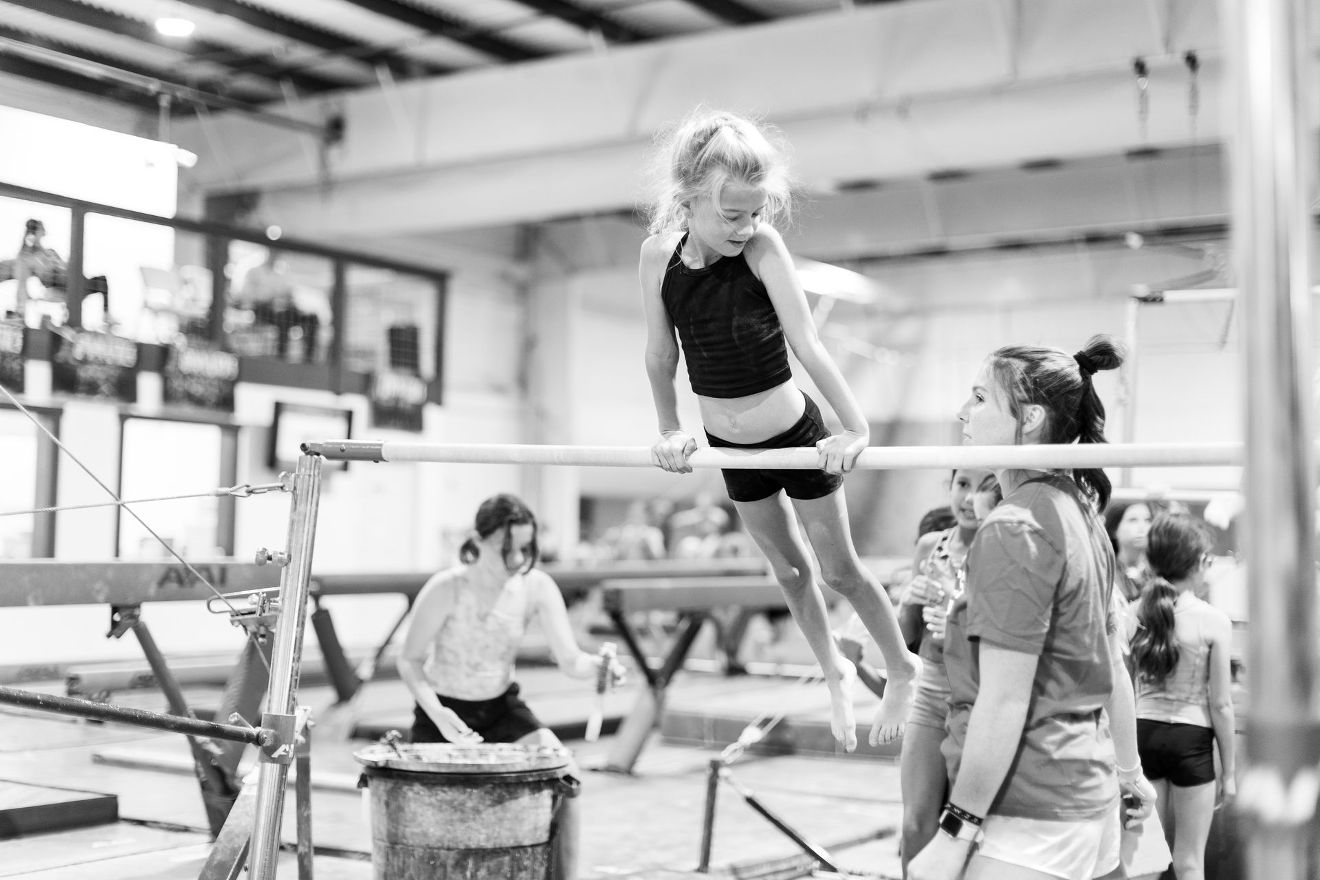 A young girl is hanging on a bar in a gym.