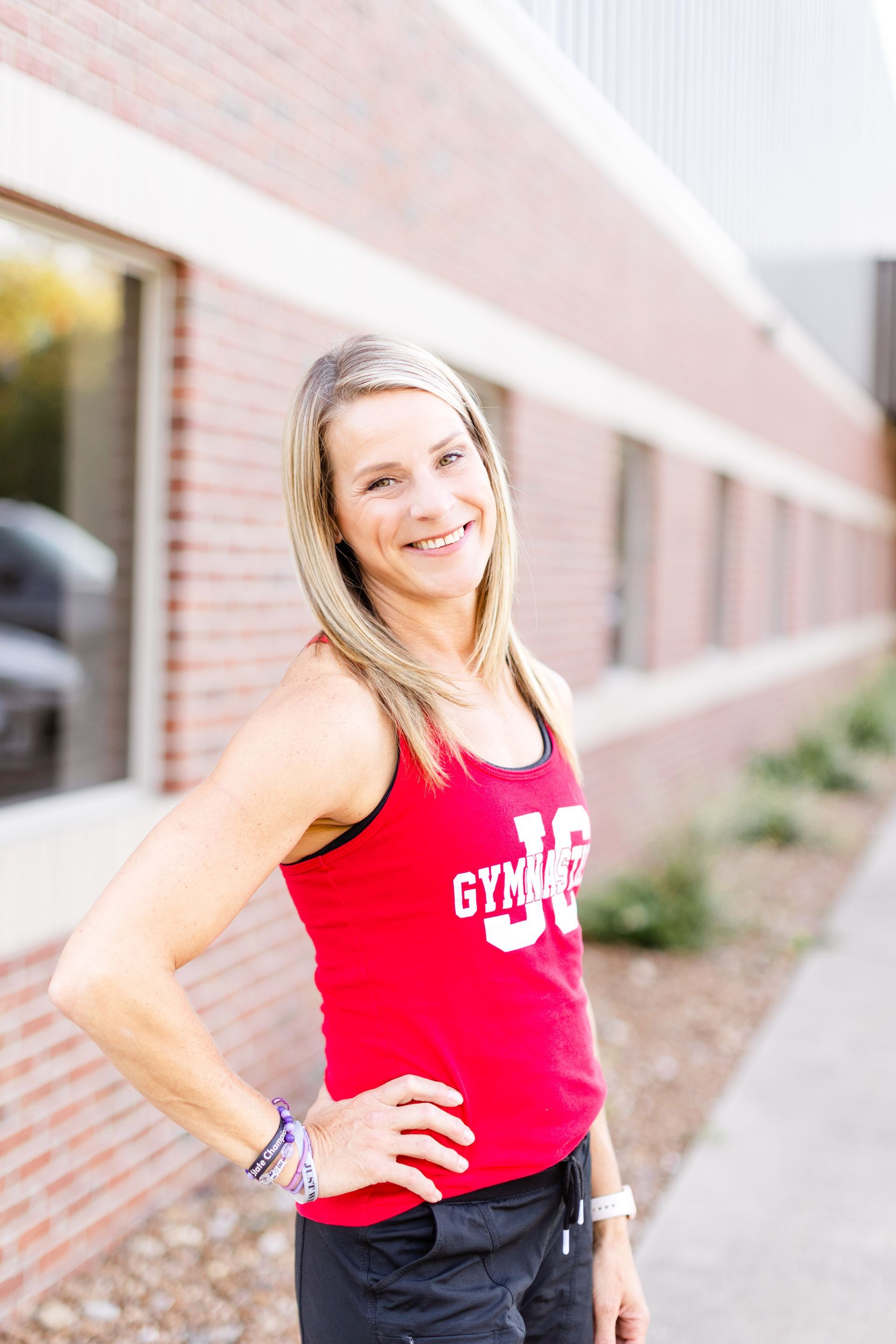 A woman wearing a red tank top is standing in front of a brick building.
