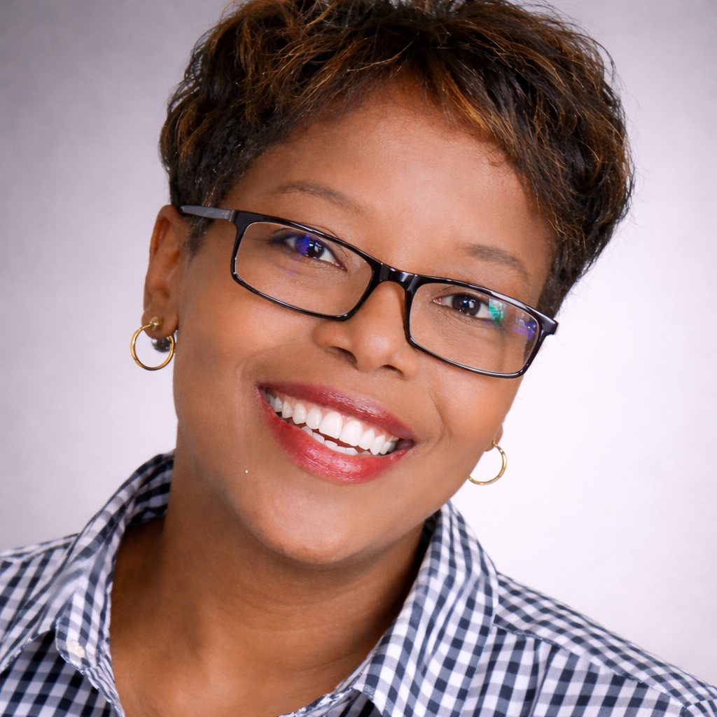 Woman with glasses smiles, wearing a checkered shirt, gold earrings in business for herself, but a part of a community.