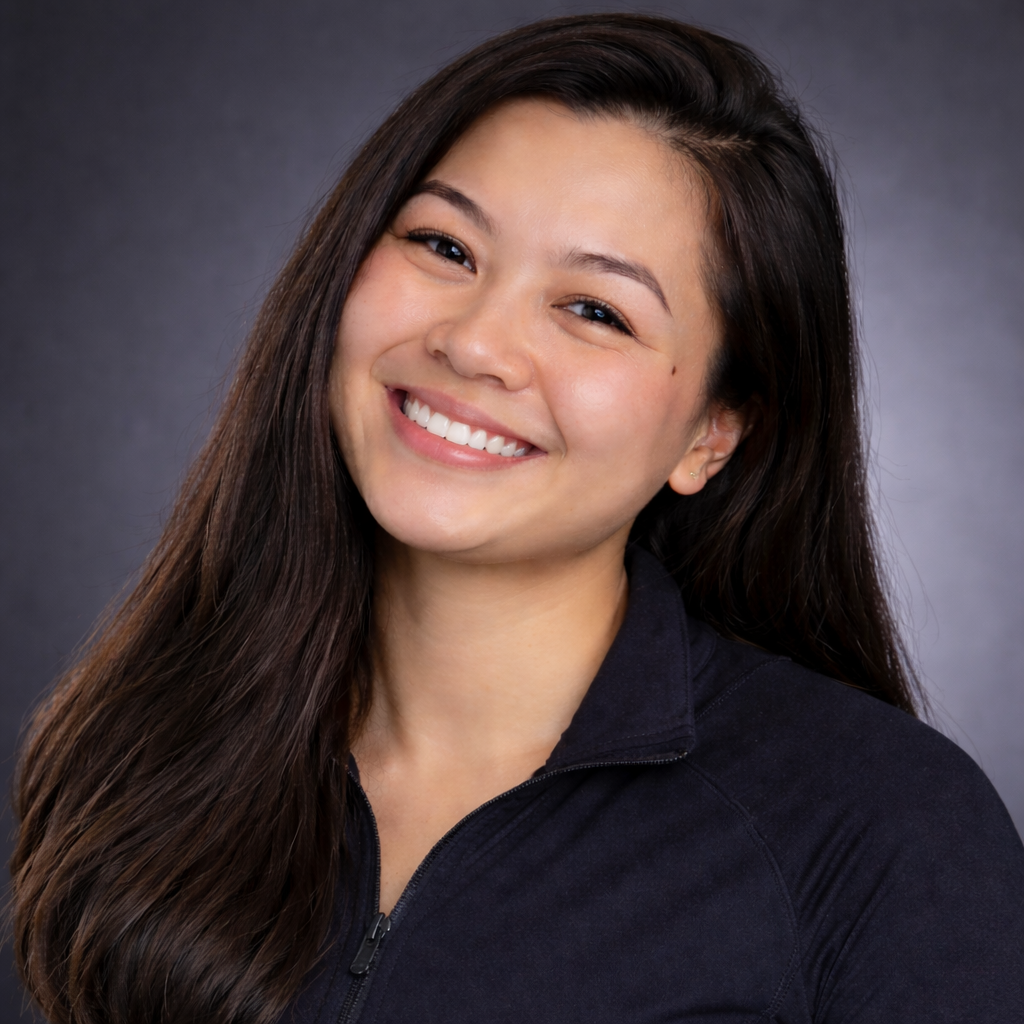 Woman with long dark hair smiles at the camera, wearing a dark top against a gray backdrop.