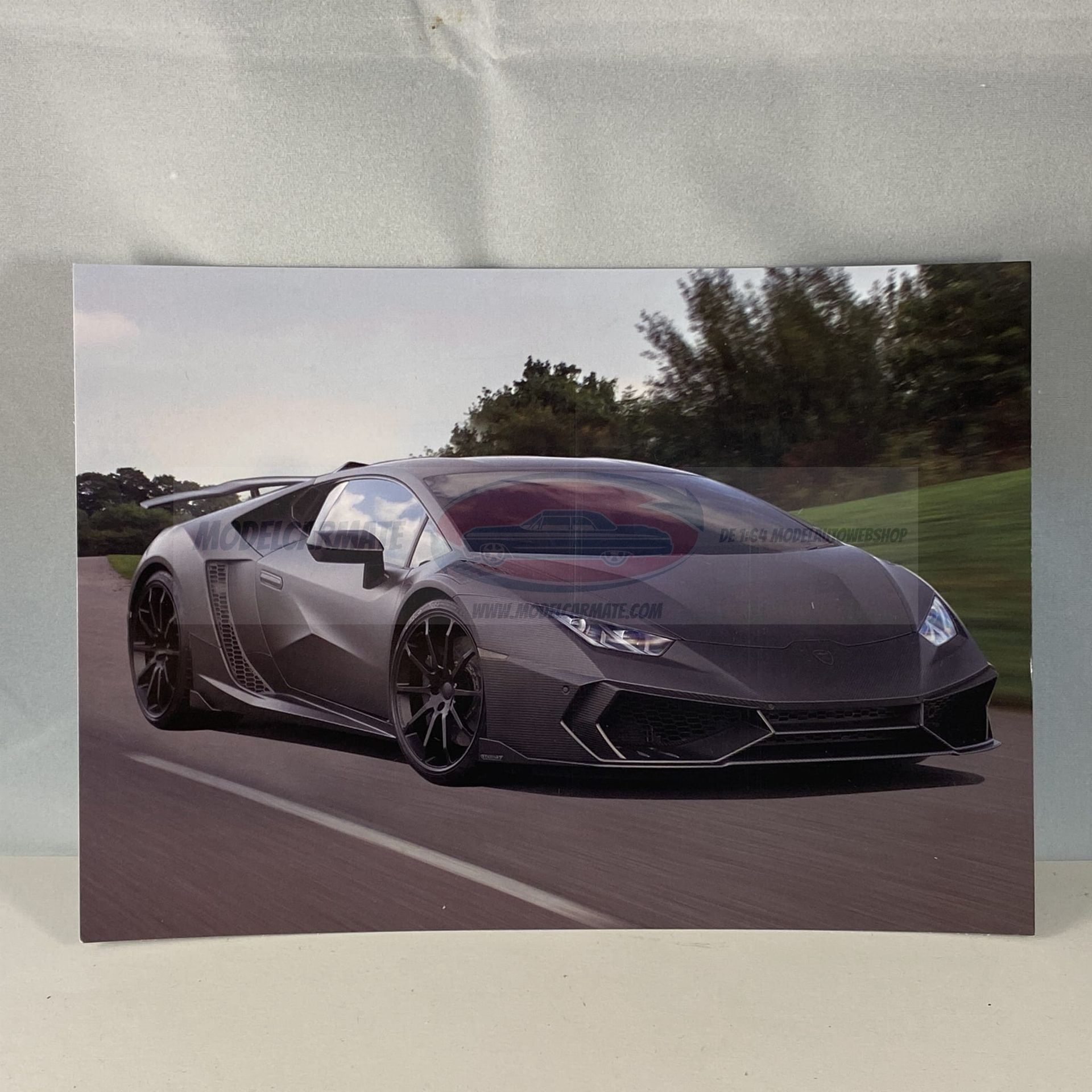 Een grijze Lamborghini Huracan sportwagen rijdt over een weg met bomen op de achtergrond.