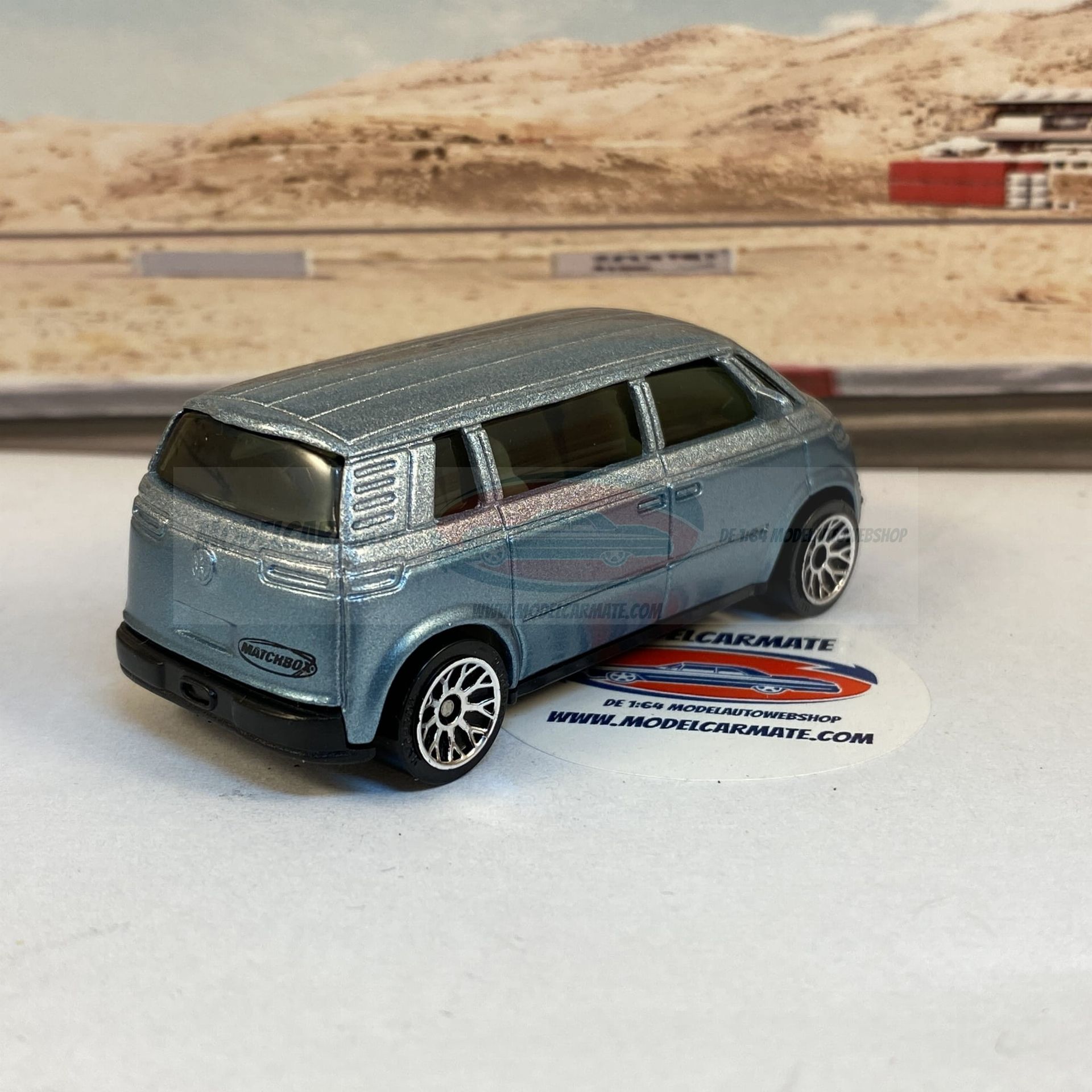 Gegoten metalen lichtblauwe bestelwagen op een witte ondergrond met een wazige buitenachtergrond.