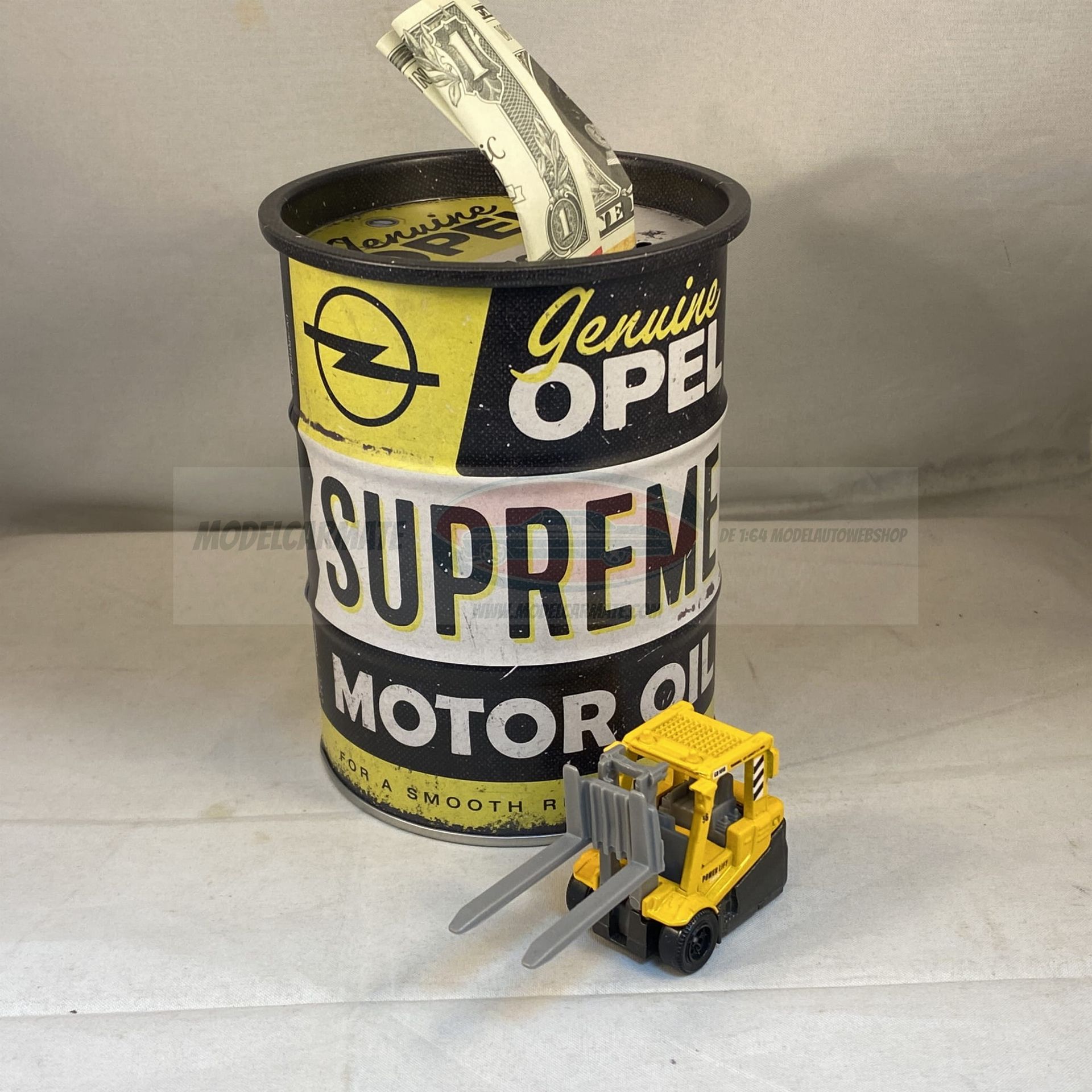 Een gele Opel-oliekan met een muntstuk dat eruit steekt, naast een gele speelgoedvorkheftruck.