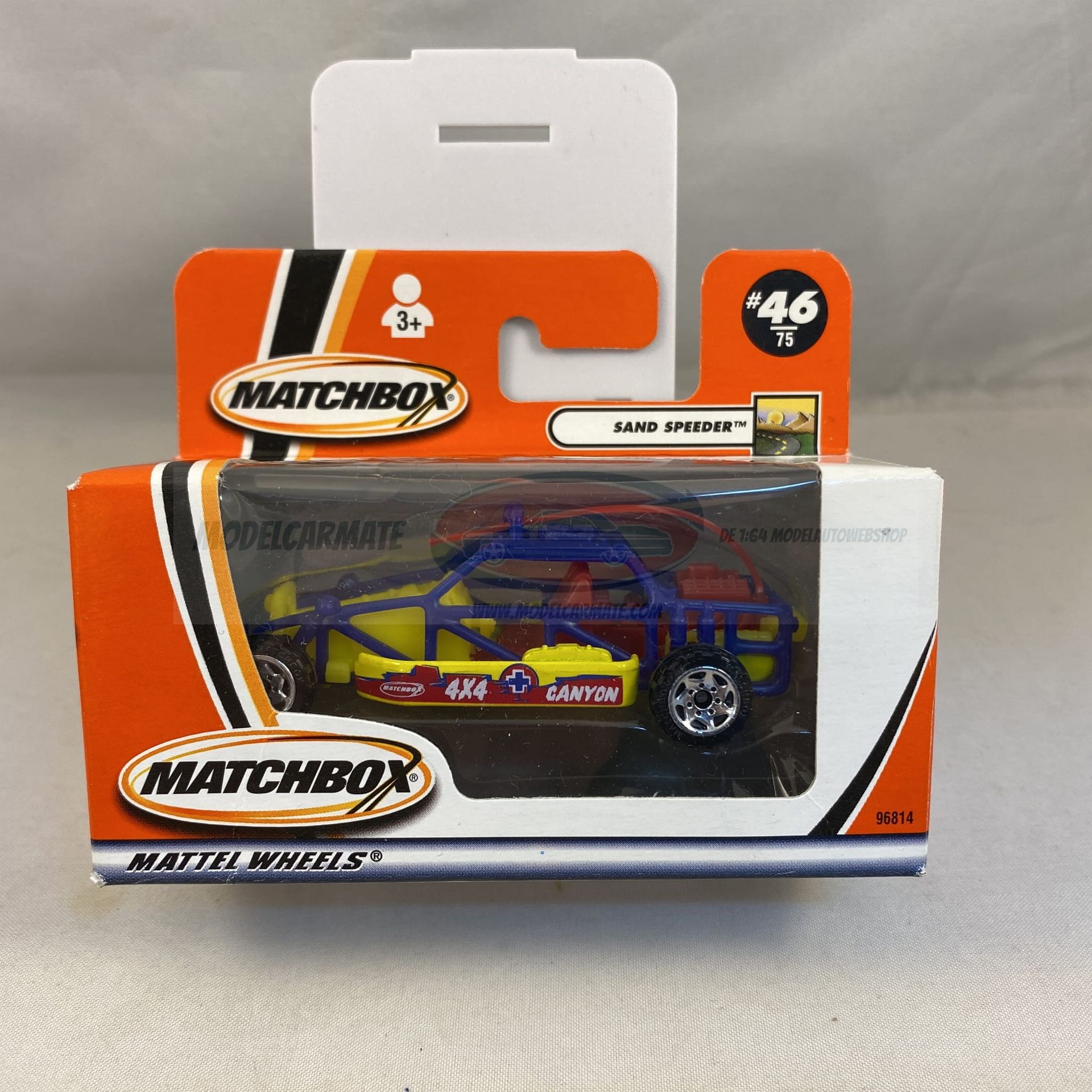 Matchbox speelgoedauto in verpakking, blauw en geel, met rolkooi, oranje en witte doos.