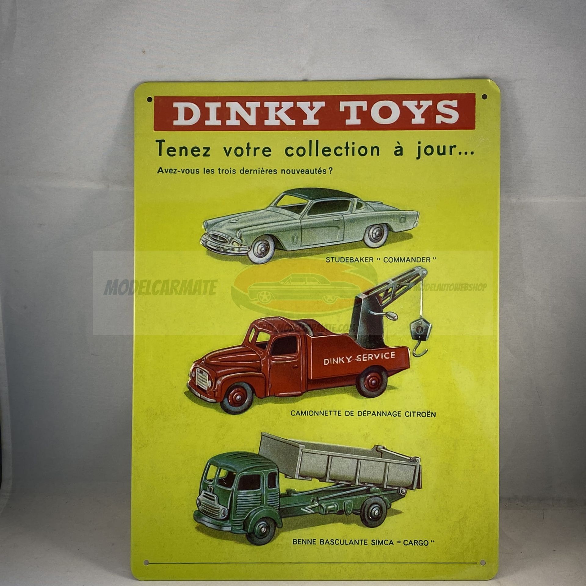 Reclame voor Dinky Toys: een geel bord met afbeeldingen van speelgoedauto's en een rode banner met de tekst 