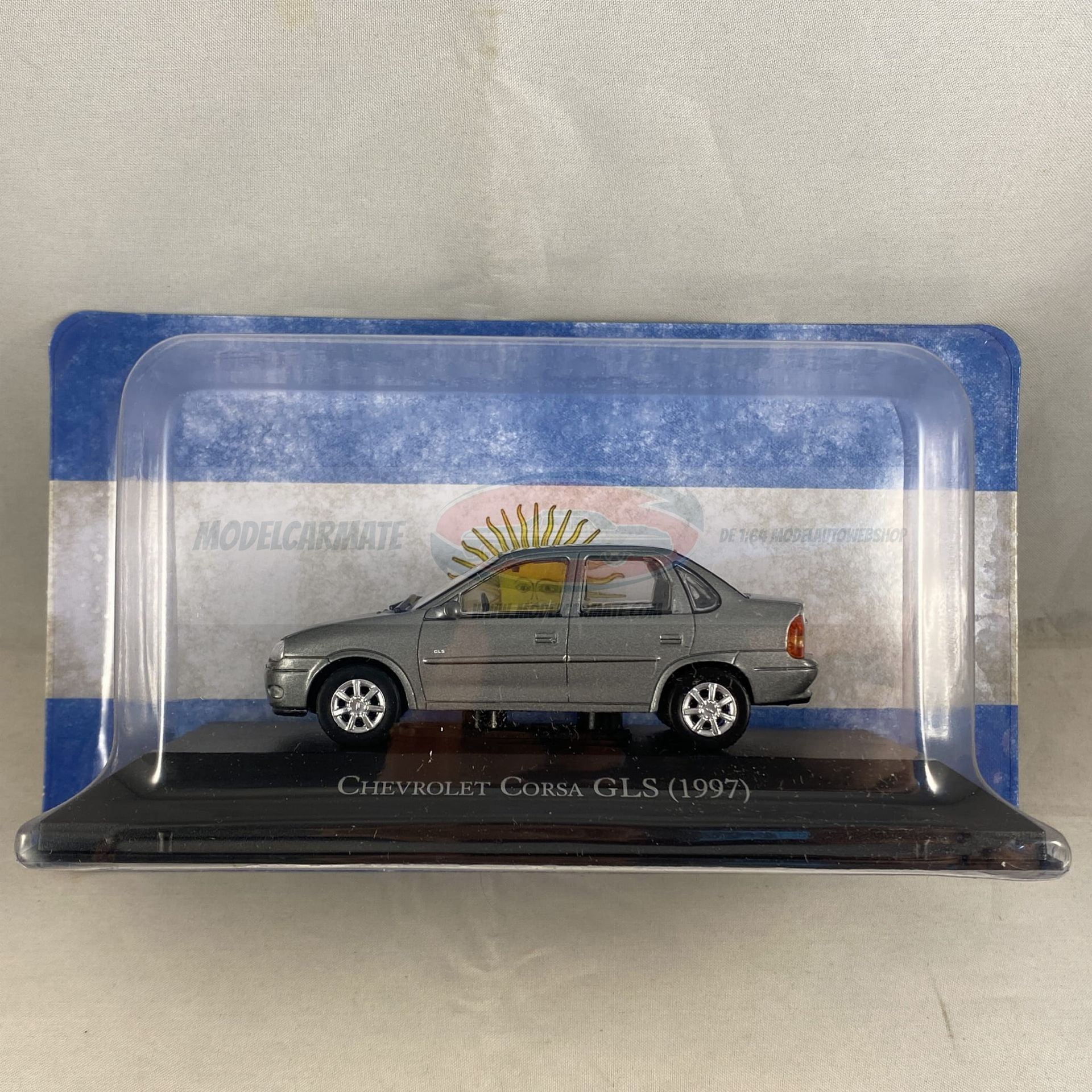 Zilverkleurige Chevrolet Corsa GLS (1998) modelauto in een vitrine. Op de achtergrond is de Argentijnse vlag te zien.
