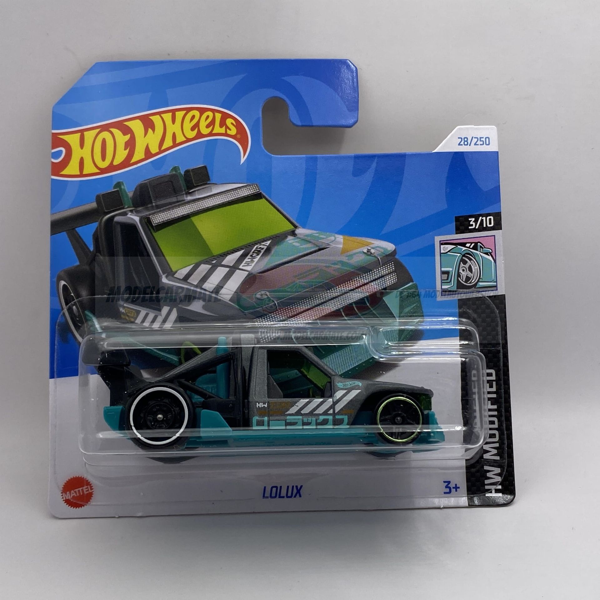 Hot Wheels speelgoedauto in verpakking, grijs en turquoise, met de tekst "Hilux Modified" op de verpakking.