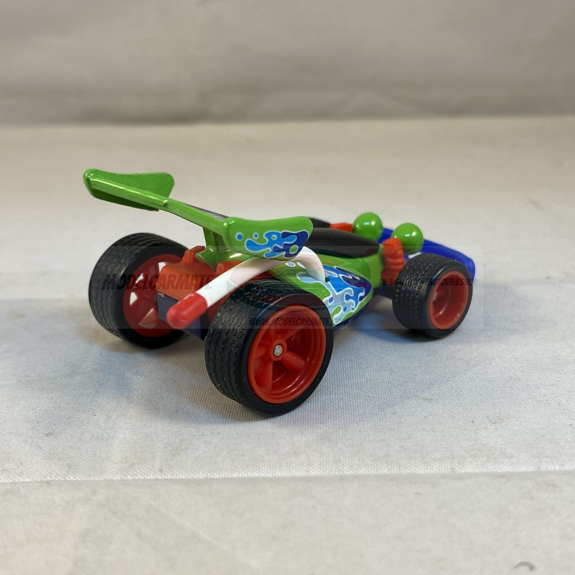 Groene speelgoedauto met kikkerachtige kenmerken, blauwe accenten en een achterspoiler.