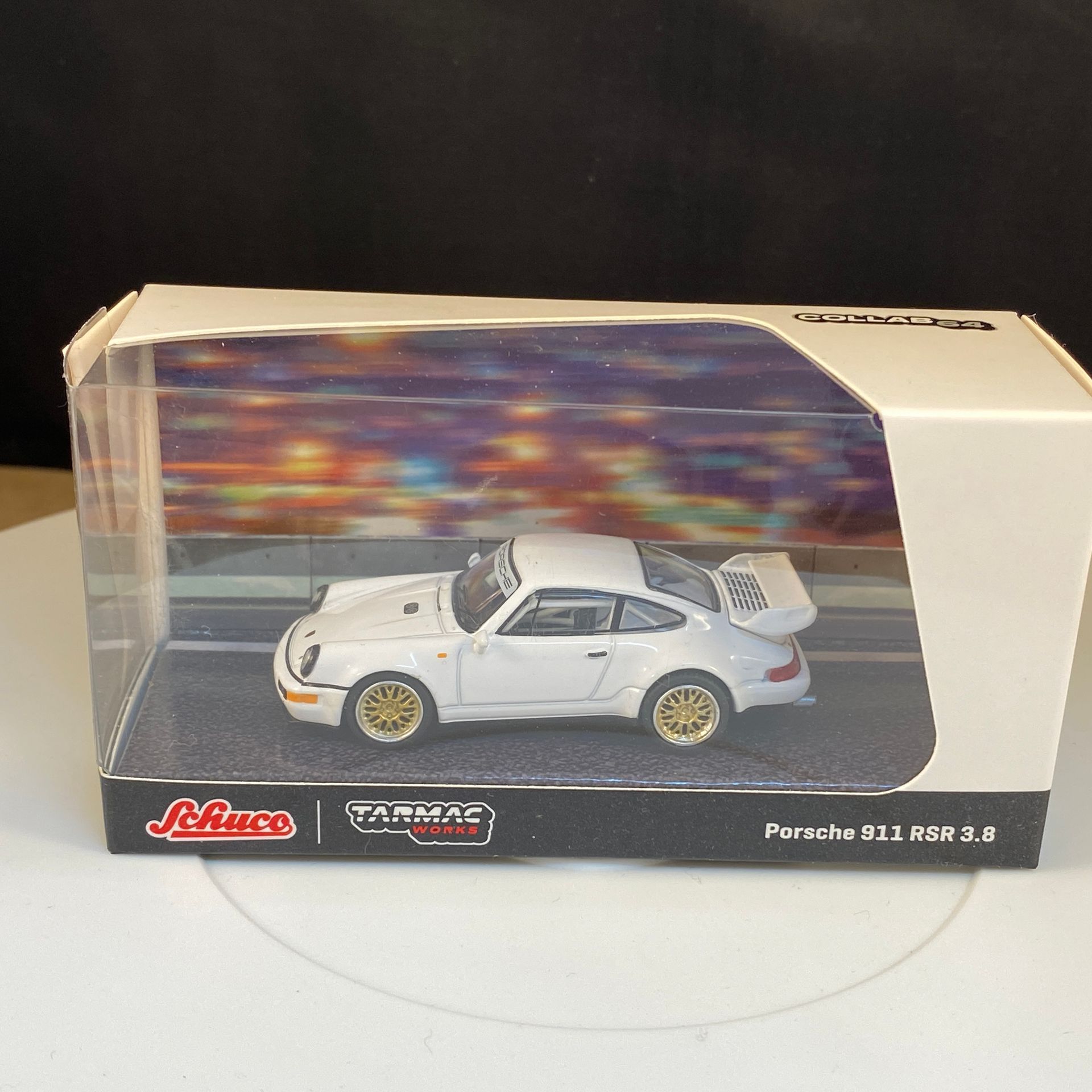 Witte Porsche 911 modelauto met gouden velgen, in een vitrine met een achtergrond van een nachtelijk straatbeeld.