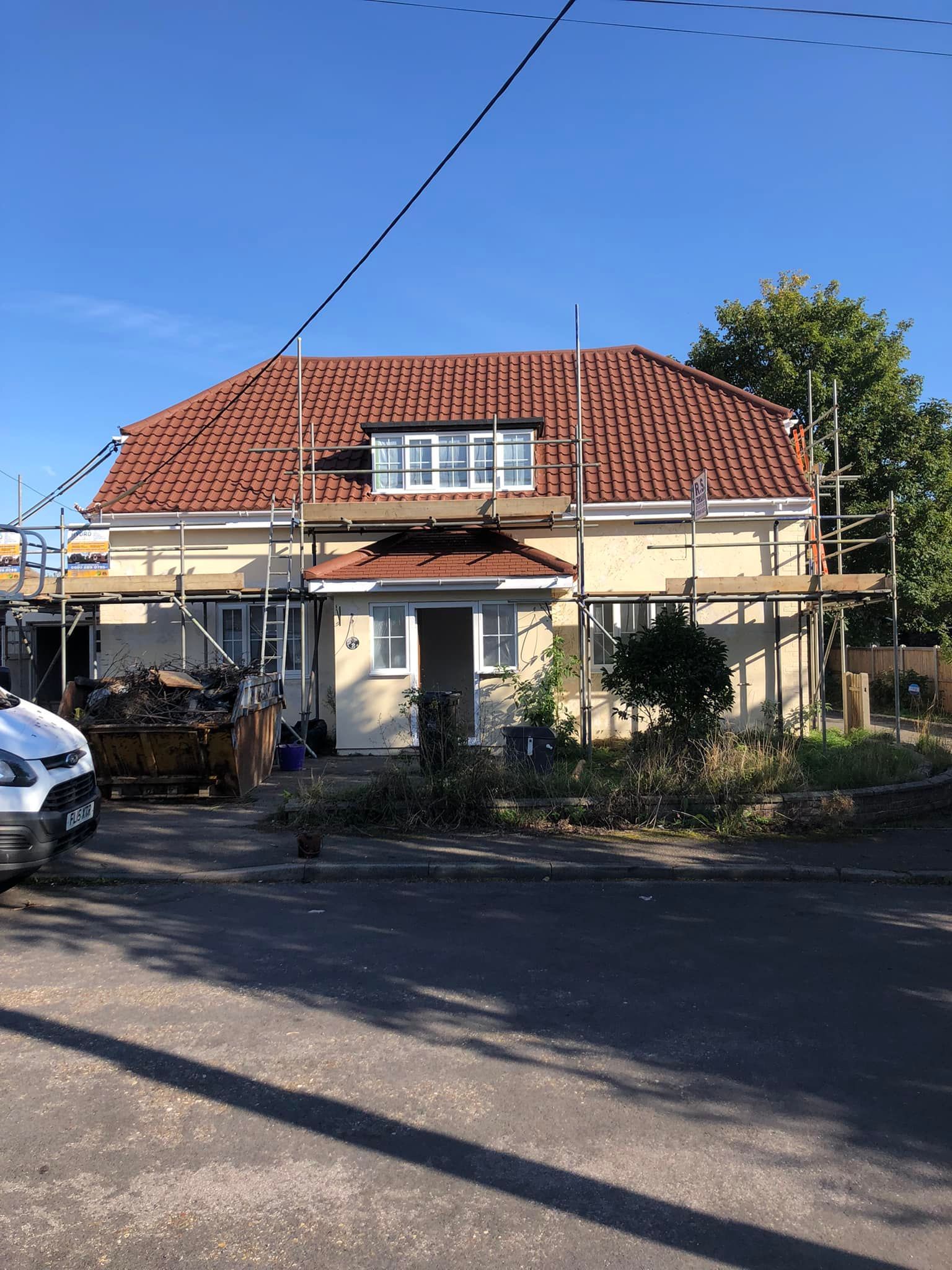A white van is parked in front of a house with scaffolding on the roof.