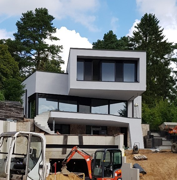 Modernes graues Haus im Bau, davor Bagger und Baumaterialien.