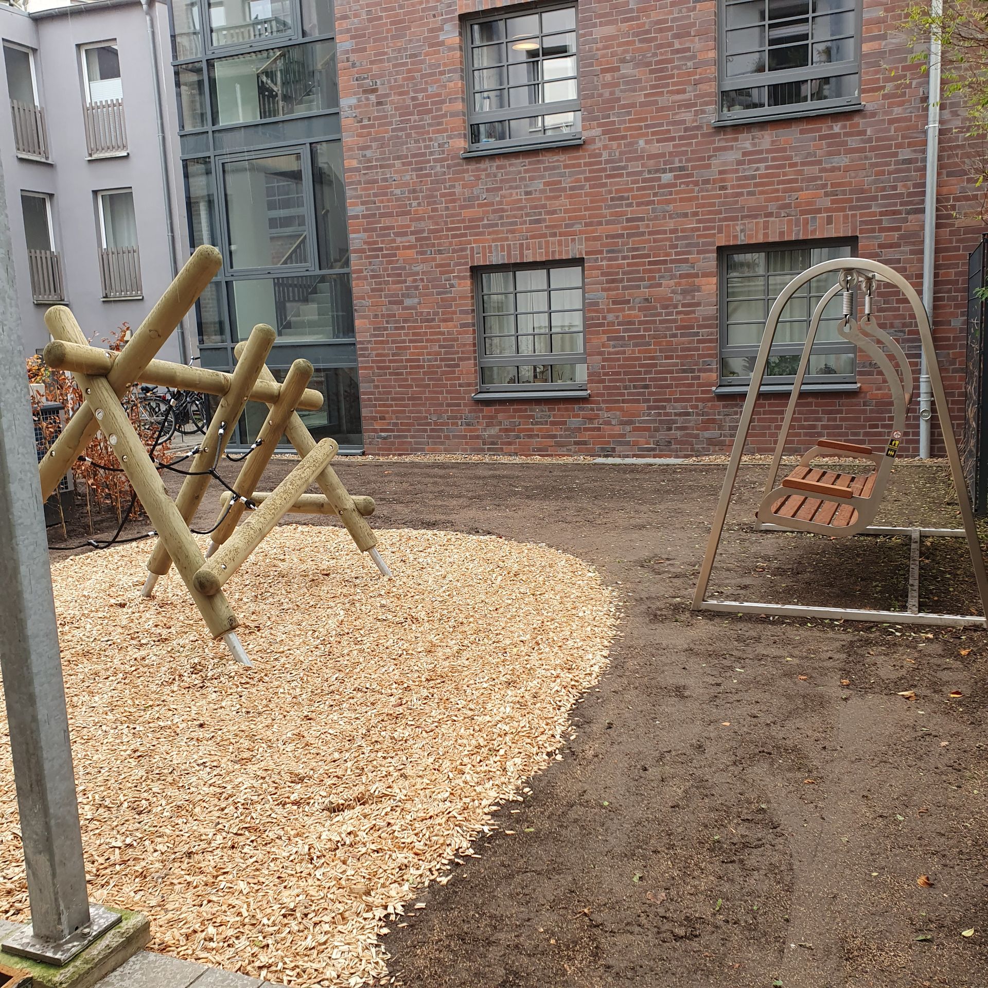 Spielplatz mit Klettergerüsten und Holzschnitzeln neben einem Backsteingebäude