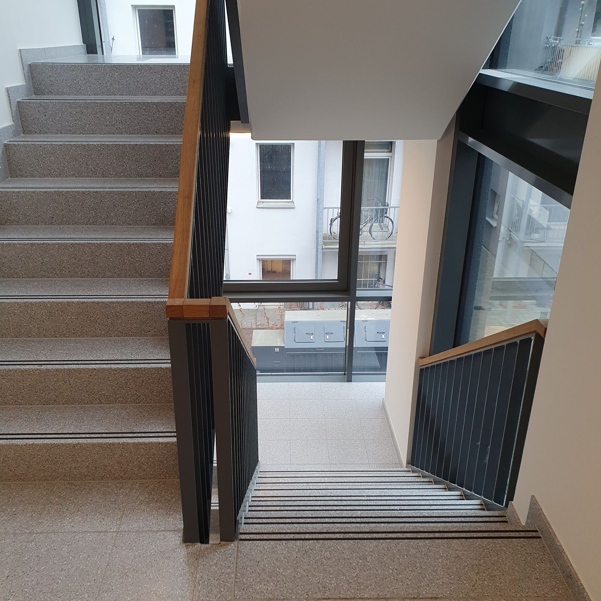 Innentreppenhaus mit einem Podest, Metallgeländer und Stufen, die zu einem tiefer gelegenen Innenhof hinunterführen.