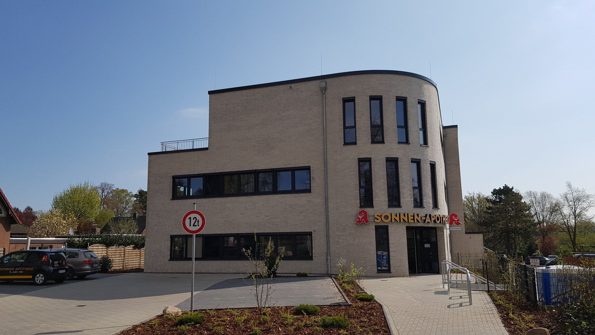 Modernes beigefarbenes Bürogebäude mit geschwungener Fassade, großen Fenstern und gepflastertem Eingang unter klarem Himmel