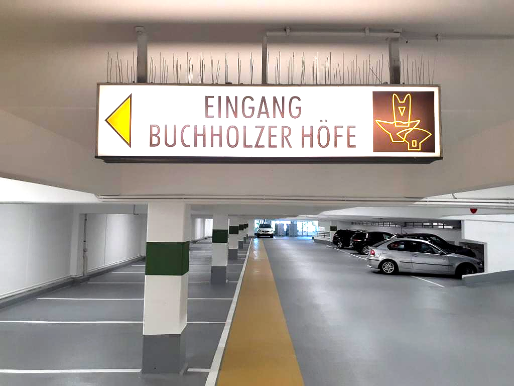 Tiefgarage mit einem Schild mit der Aufschrift „Eingang Buchholzer Höfe“ und geparkten Autos auf der rechten Seite.