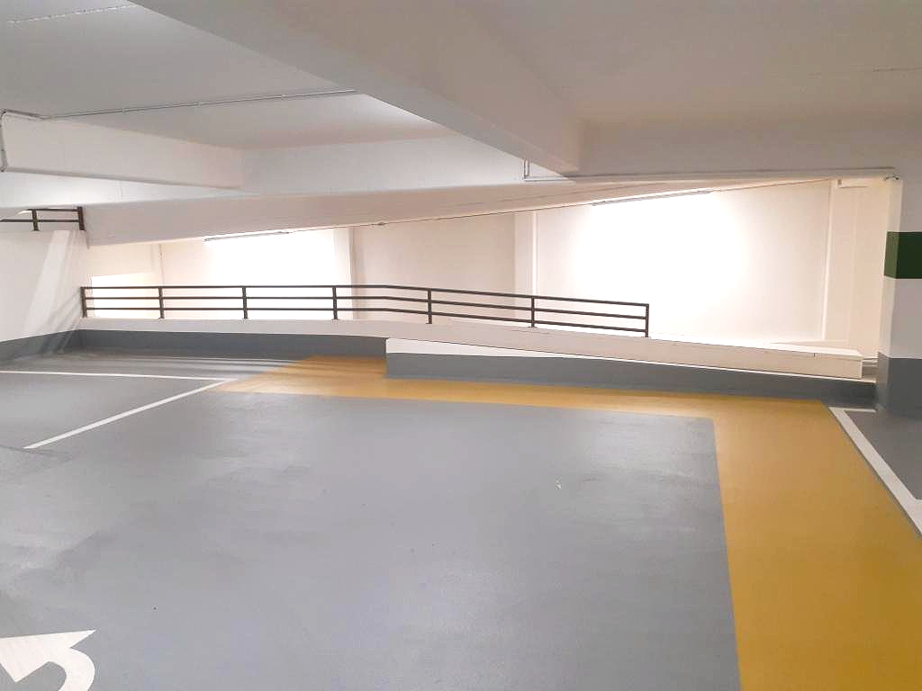Leere Parkgaragenrampe mit gelben Fahrbahnmarkierungen und einem Metallgeländer entlang der Wand