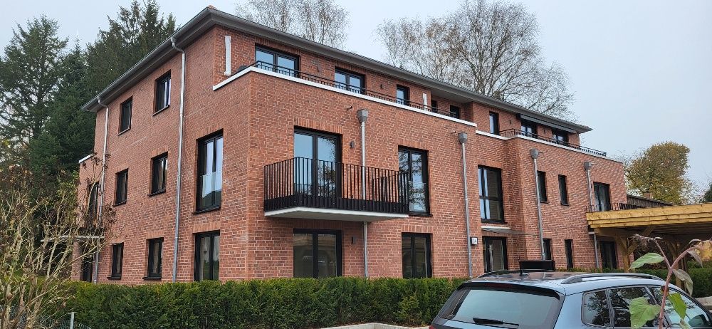 Dreistöckiges, rotes Backstein-Wohnhaus mit Balkonen und davor geparkten Autos.