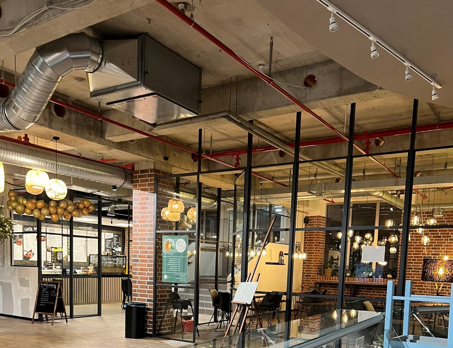 Café-Interieur im Industriestil mit freiliegenden Rohren, Glastrennwänden und warmen Hängeleuchten