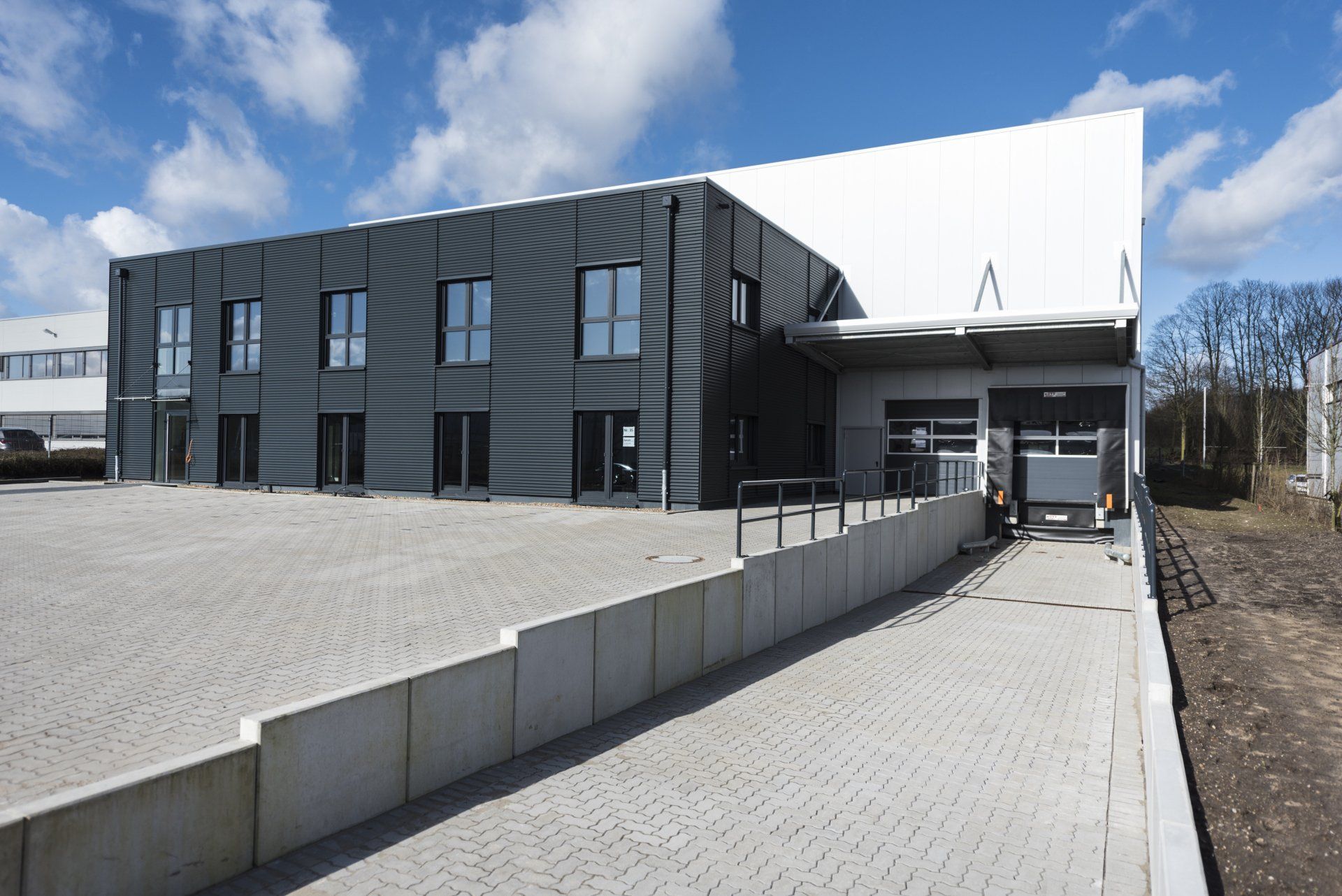 Modernes schwarzes Gebäude mit gepflasterter Auffahrt und Betonmauer unter klarem Himmel