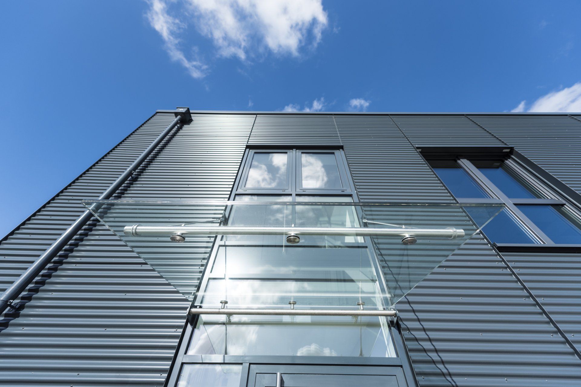 Moderne Glas- und Metallfassade vor blauem Himmel mit Wolken
