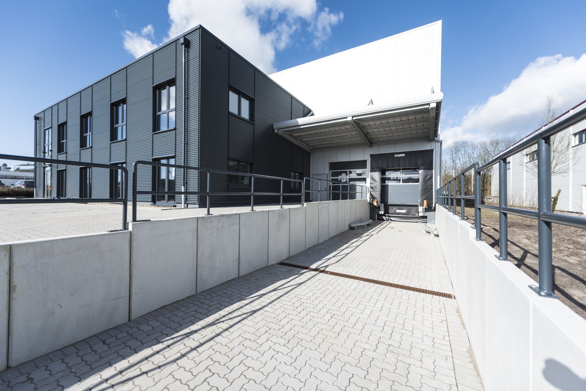 Moderner Gebäudeeingang mit gepflastertem Gehweg, Glasgeländer und strahlend blauem Himmel