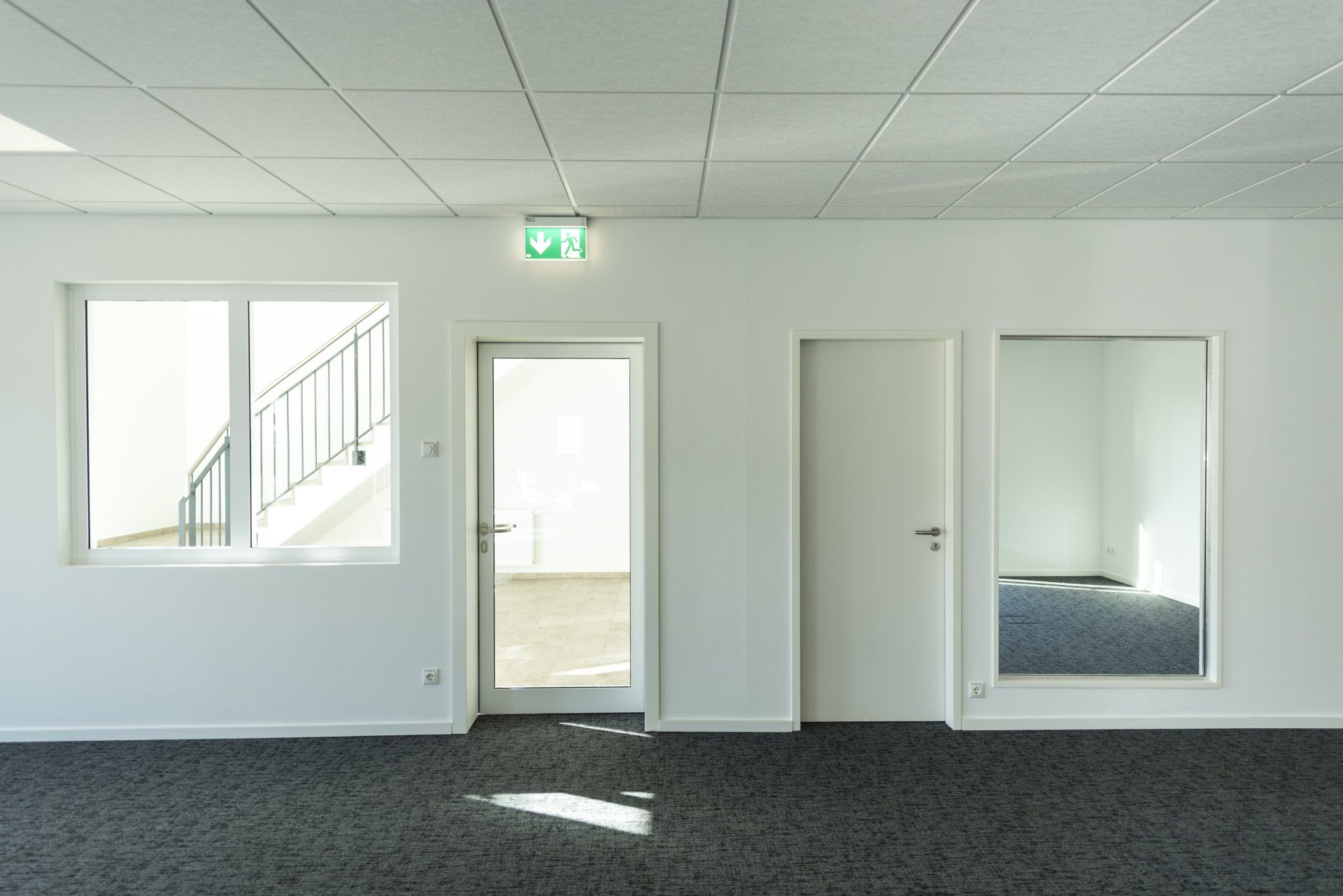 Leeres weißes Zimmer mit grauem Teppichboden, Fenstern, offener Tür und Spiegelschranktüren