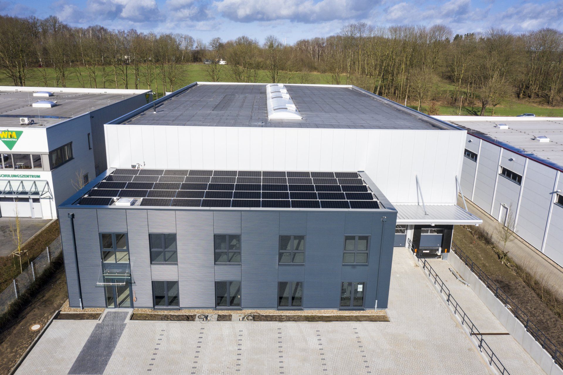 Luftaufnahme eines modernen Industriegebäudes mit großem weißen Dach und grauer Fassade.