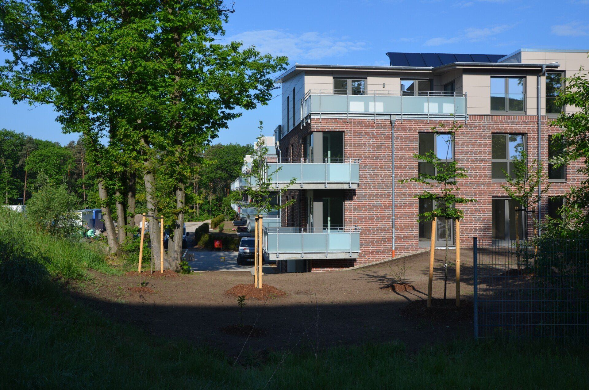Modernes Backstein-Mehrfamilienhaus mit Balkonen neben Bäumen und einem begrünten Innenhof
