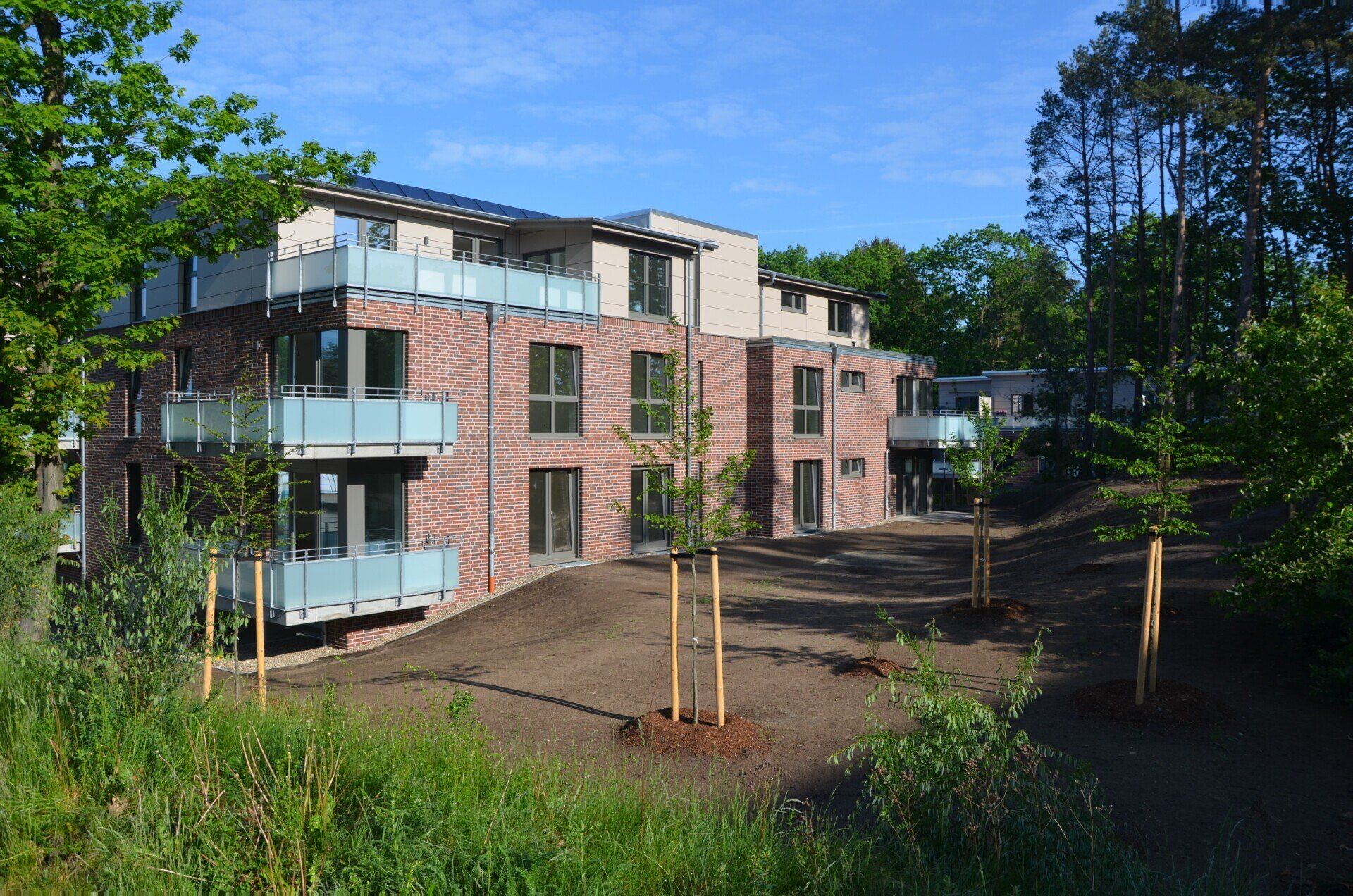 Modernes Backstein-Mehrfamilienhaus mit Balkonen, umgeben von Bäumen und einem unbefestigten Innenhof