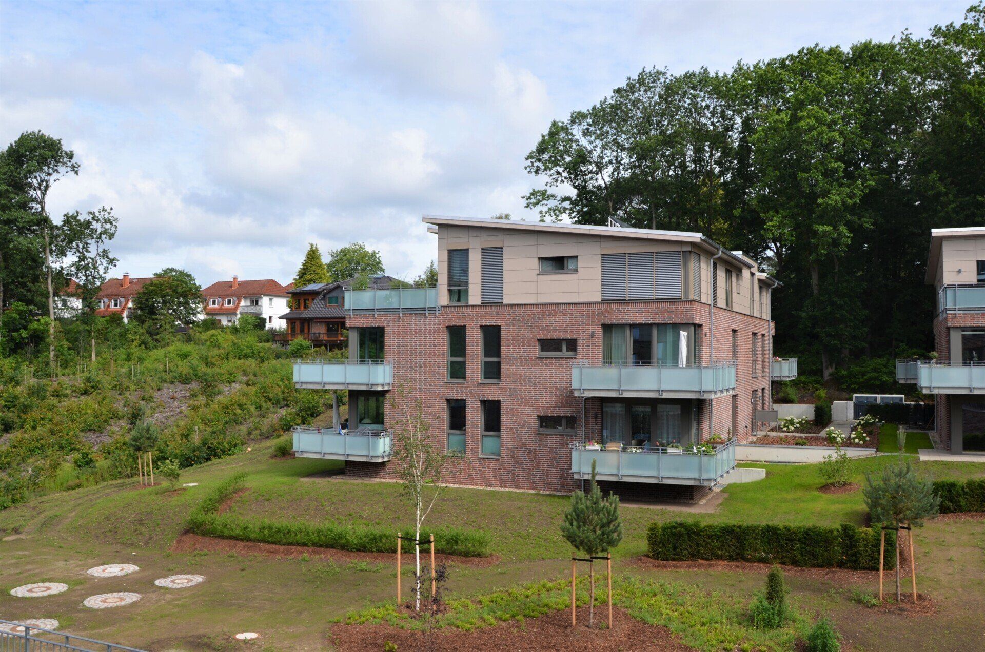 Modernes Backstein-Apartmentgebäude mit Balkonen, die auf einen begrünten Innenhof unter einem bewölkten Himmel blicken
