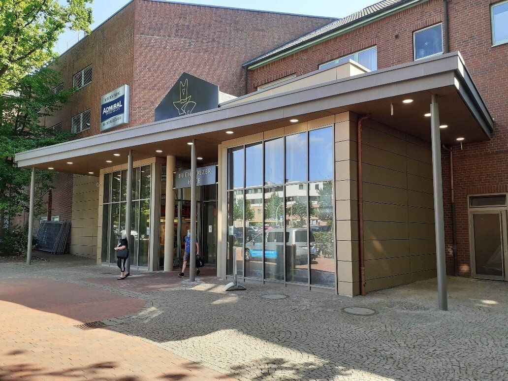 Moderner Eingang zu einem Backsteingebäude mit Glastüren, großen Fenstern und einer überdachten Markise.