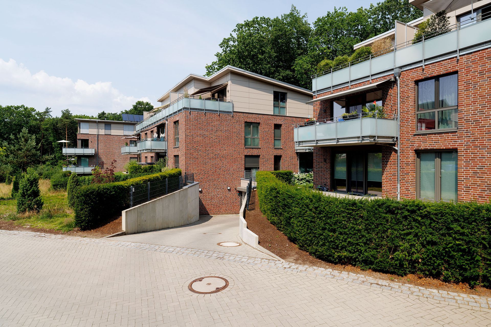 Moderne Backstein-Apartmentgebäude mit Balkonen, Hecke und gepflastertem Hofeingang
