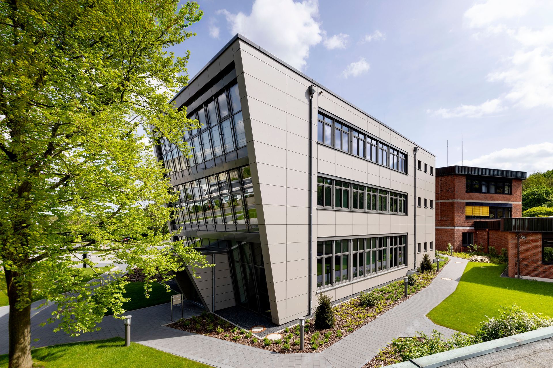Modernes Bürogebäude mit großen Fenstern, grünem Rasen und Bäumen an einem sonnigen Tag