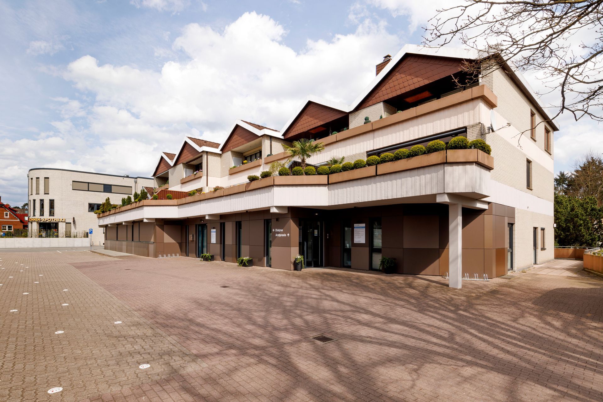 Modernes Wohnhaus mit Balkonen und gepflastertem Innenhof unter einem teilweise bewölkten Himmel