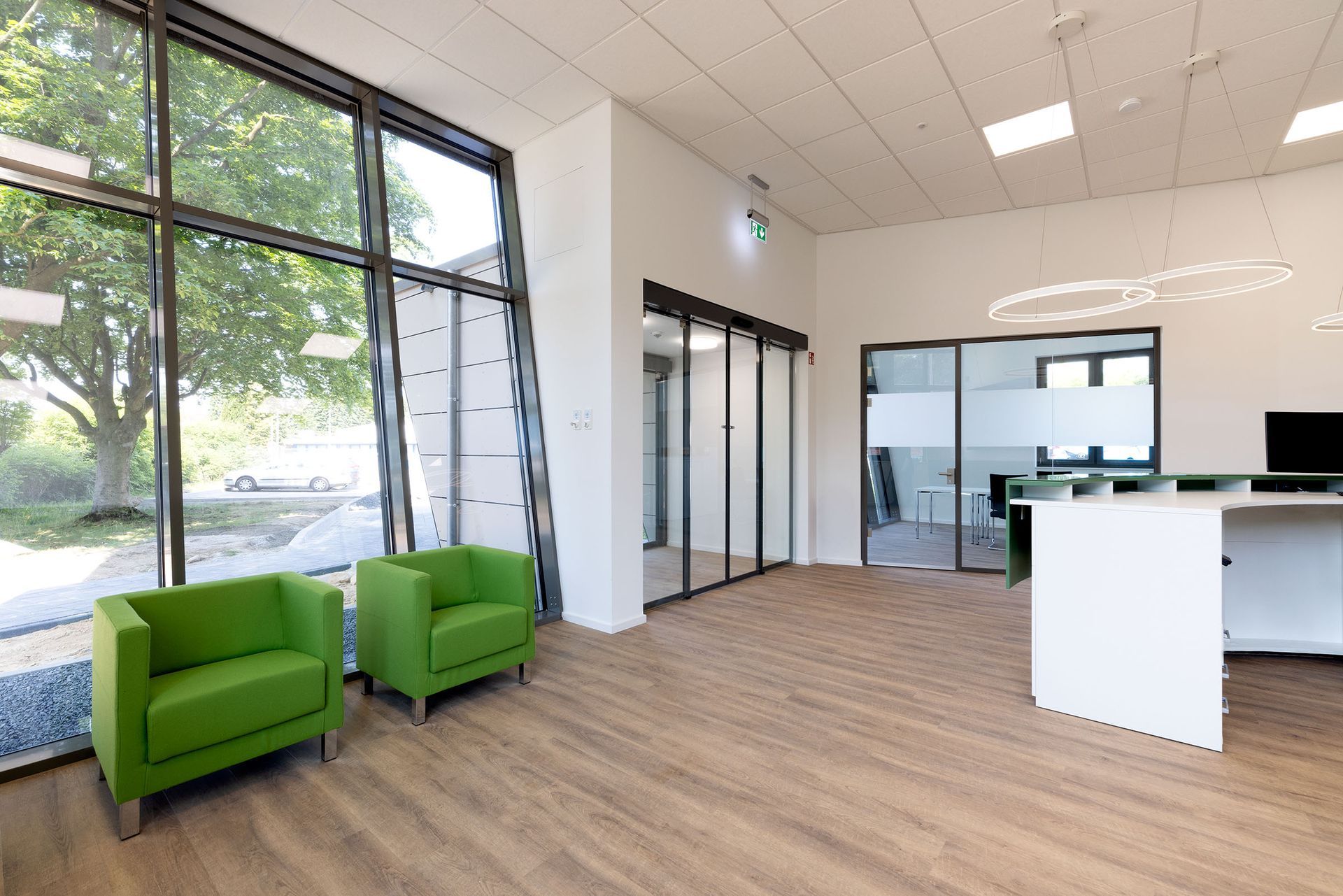 Moderne Bürolounge mit grünen Stühlen, großen Fenstern, Glastüren und einem Empfangstresen