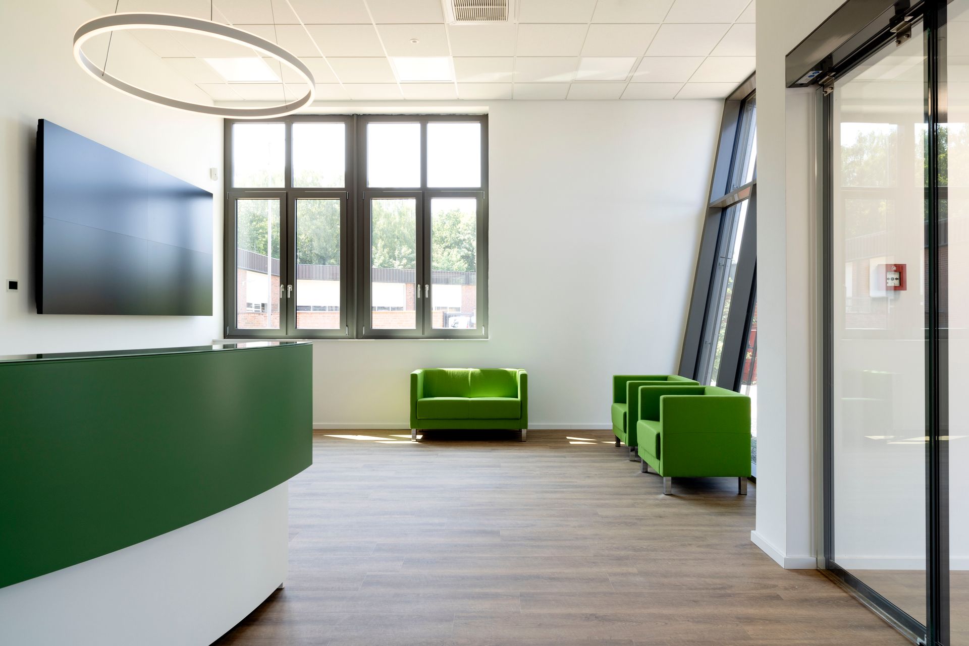 Moderne Bürolobby mit grünen Stühlen, geschwungenem weißen Schreibtisch, großen Fenstern und Glastür