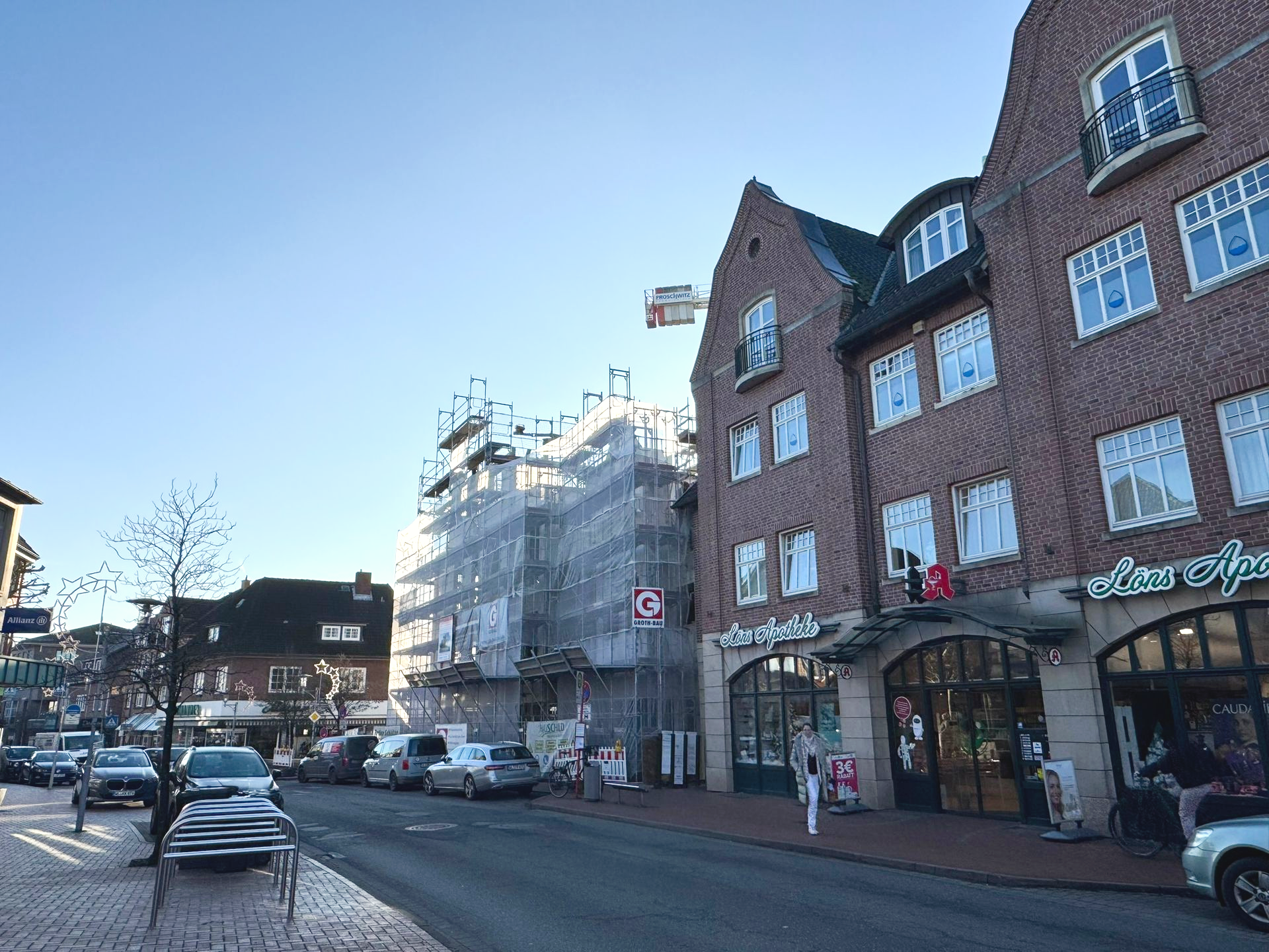Straße mit Backsteingebäuden, geparkten Autos und Baugerüsten an einem sonnigen Tag.