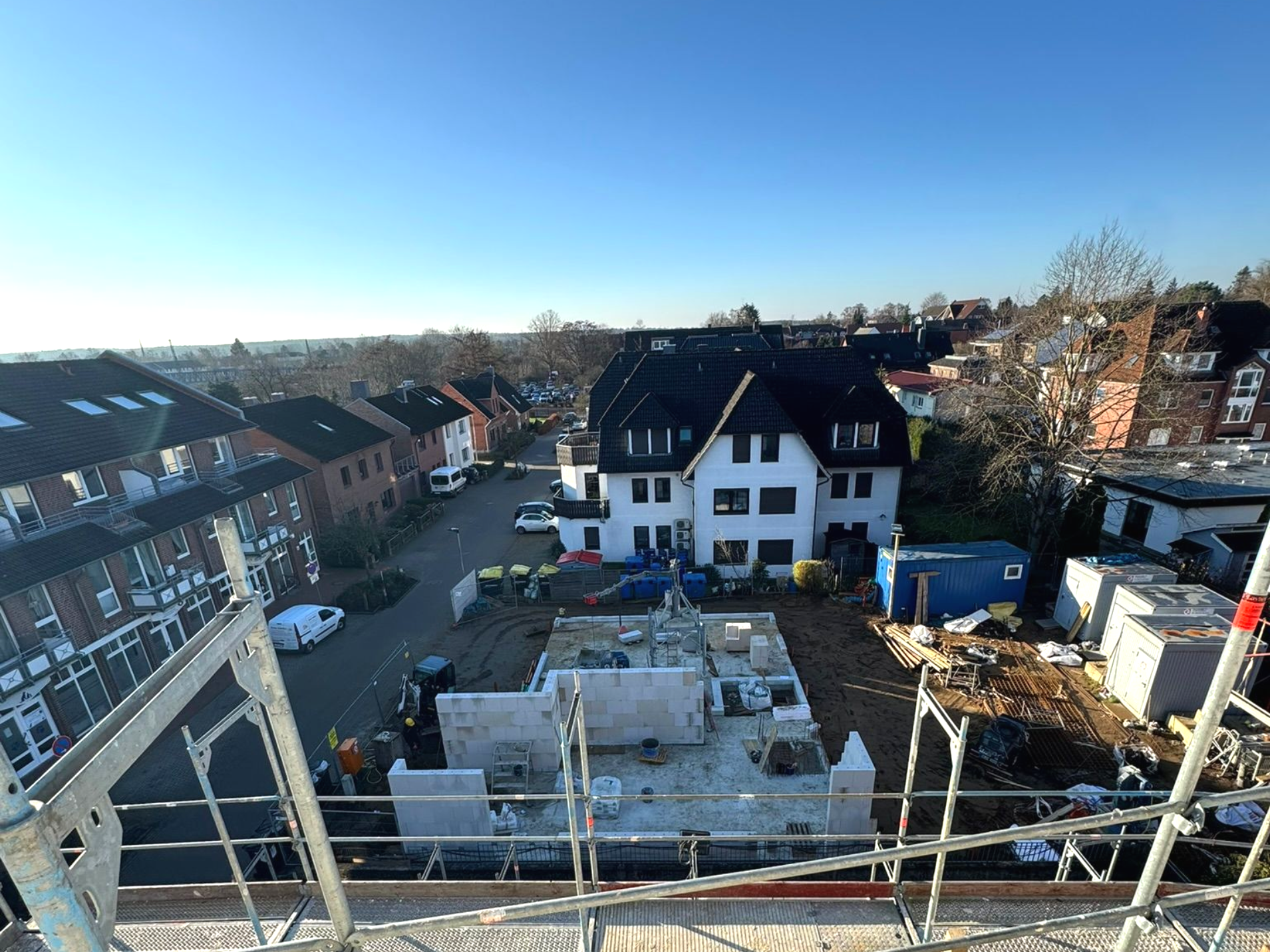 Blick von einem Dach über eine Wohnbaustelle mit Häusern und klarem blauen Himmel.