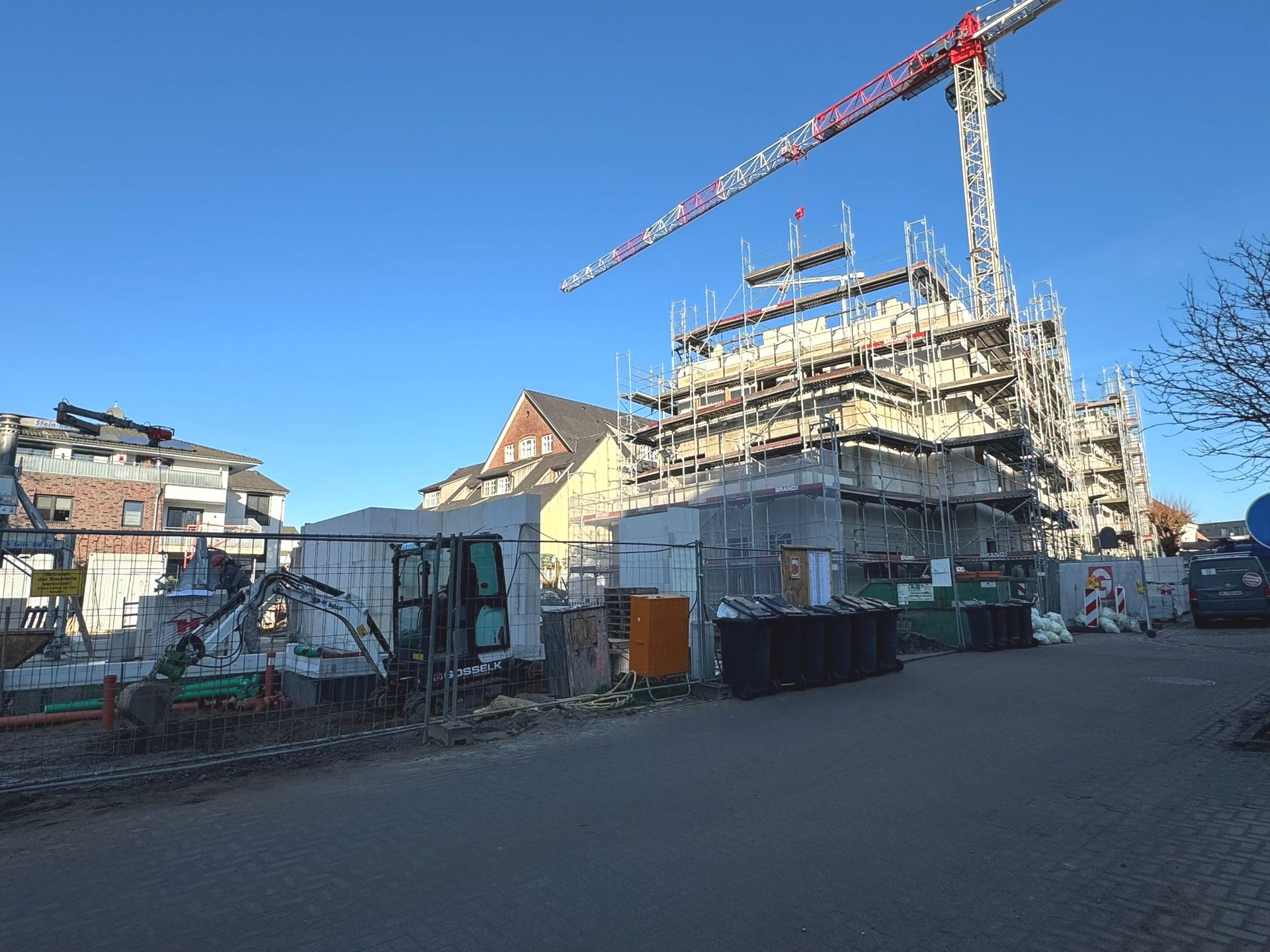 Baustelle mit einem hohen Kran, einem Gerüst und einem teilweise errichteten Bauwerk unter strahlend blauem Himmel.