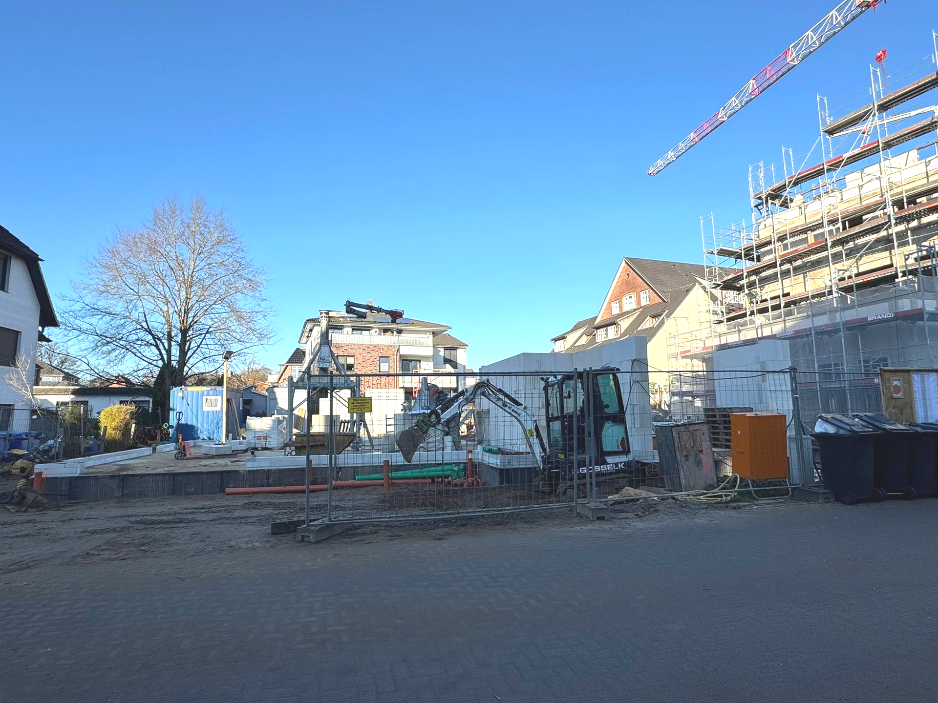 Baustelle mit Gerüsten und Kränen neben Häusern unter strahlend blauem Himmel